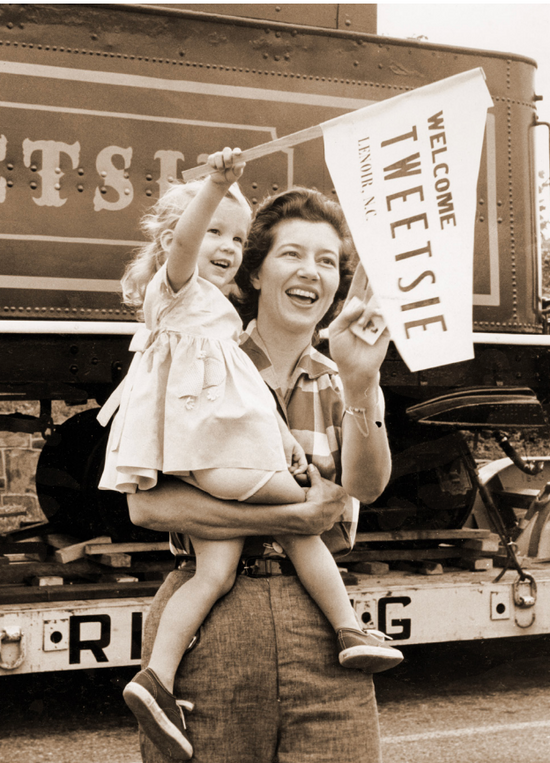 Vintage photograph of a mother and daughter welcoming the Tweetsie Railroad steam engine to Blowing Rock, NC, a beloved part of the High Country's heritage.